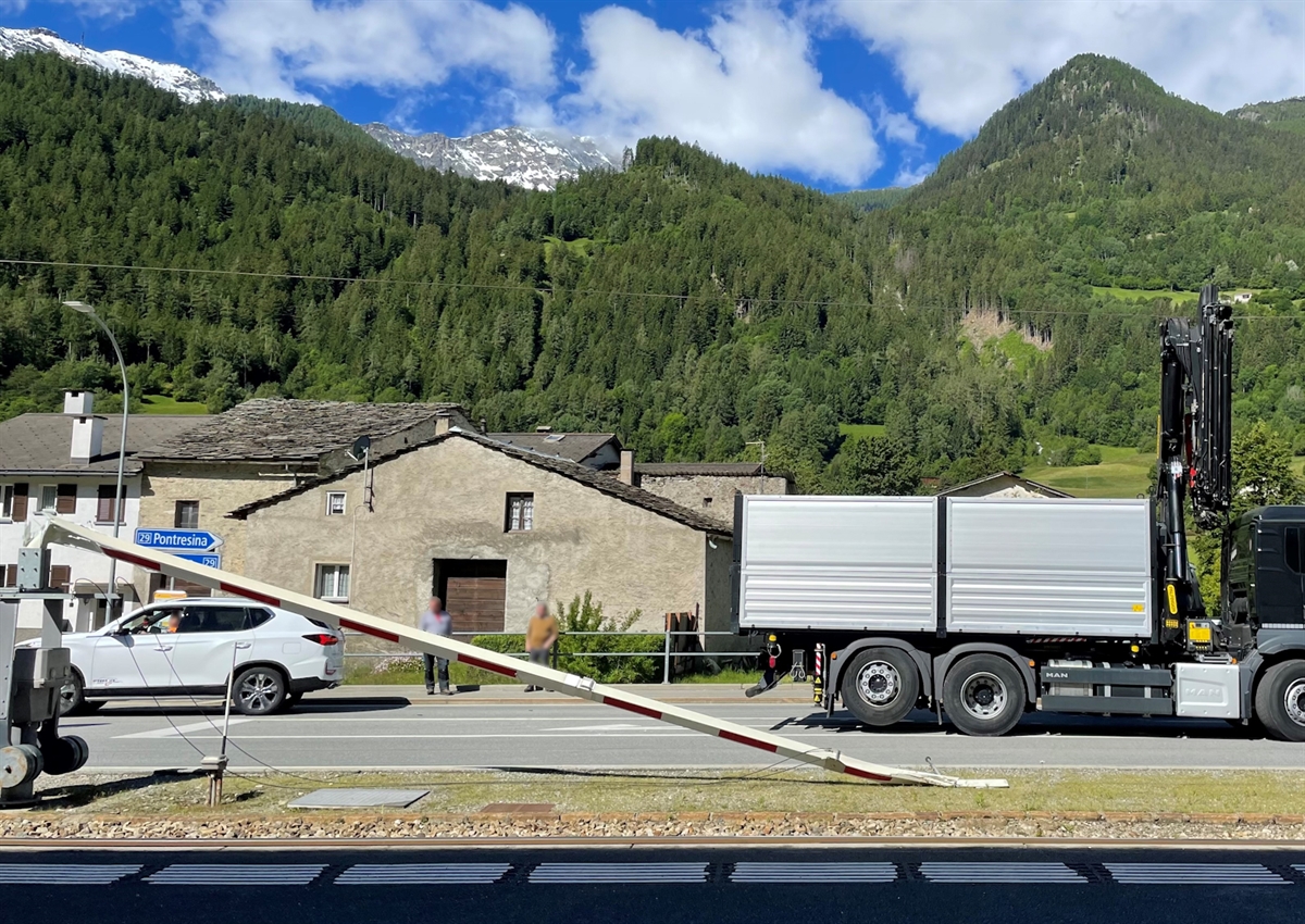 Der Lastwagen steht mit nicht restlos zusammengekappten Ladekran auf der Berninastrasse. Die Fahrleitung hängt am Kran. Im Vordergrund eine der beiden abgebrochenen Barrieren.