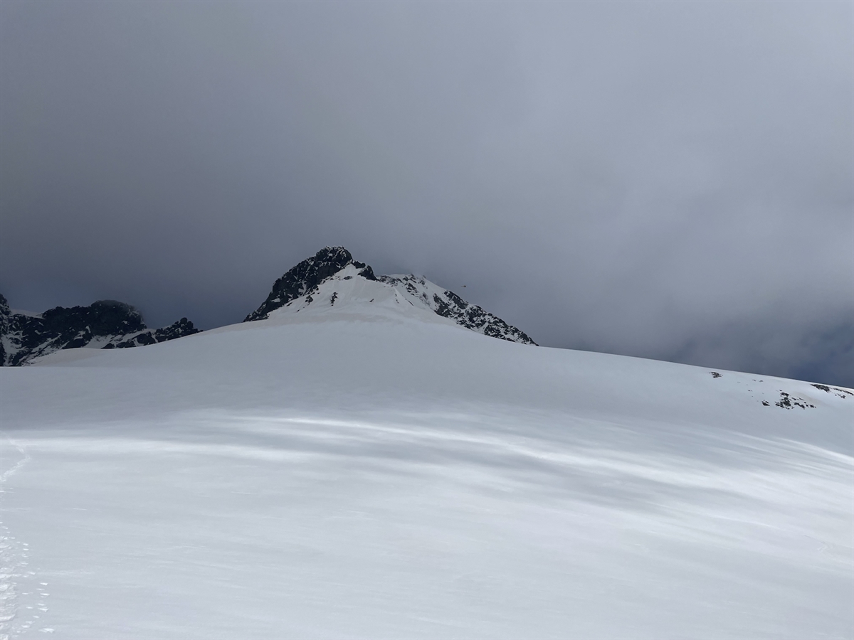 Das Schneefeld am Spallagrat im Berninagebiet. Der Piz Bernina befindet sich im Nebel. Ein Helikopter umkreist den Spallagrat.