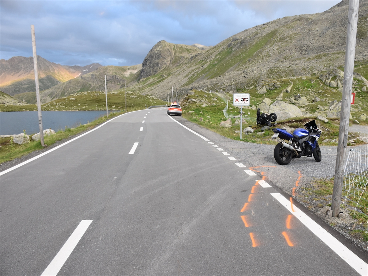 Die Flüelastrasse mit dem rechtsseitigen Ausstellplatz. Auf diesem steht das Motorrad des an ersten Stelle fahrenden Mannes. Hinter diesem liegt an einen Stein angelehnt das Motorrad des Lernfahrers.