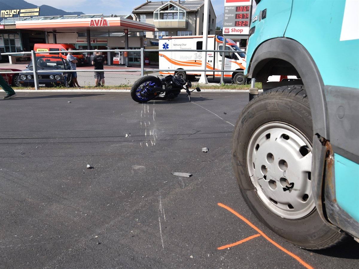 Das Motorrad liegt auf der Strasse vor dem Lieferwagen. Im Hintergrund eine Tankstelle mit drei Personen davor.