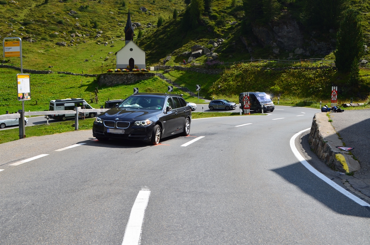 Strassenverlauf der Flüelastrasse im Bereich der Unfallstelle. Auf der linken Seite ist das beteiligte Fahrzeug zu erkennen. Im Hintergrund sind eine wartende Autokolonne und eine Kapelle zu erkennen.