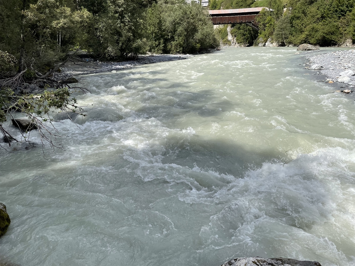 Der Flusslauf des Inns. Im Hintergrund eine darüber führende Holzbrücke.