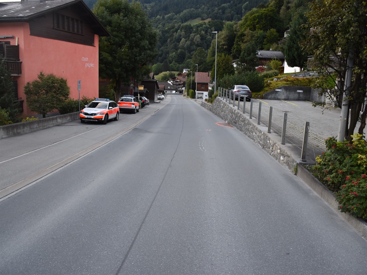 Die abfallende Landstrasse. Links auf einem Parkplatz 2 Polizeiautos. Auf der Strasse Bremsspuren des Velos.