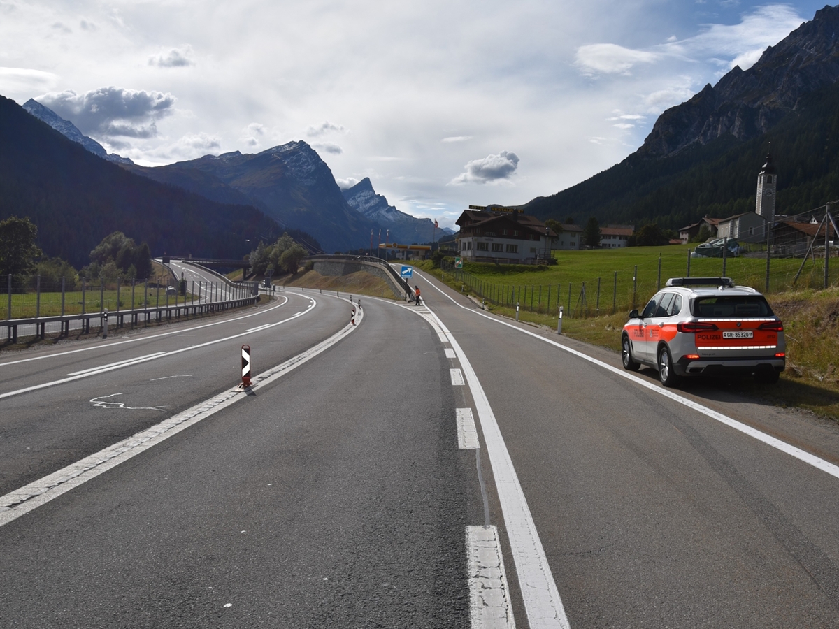 Rechts ein Polizeiauto. In Bildmitte die Trenninsel. Im Hintergrund Berge und leicht bewölkter Himmel.