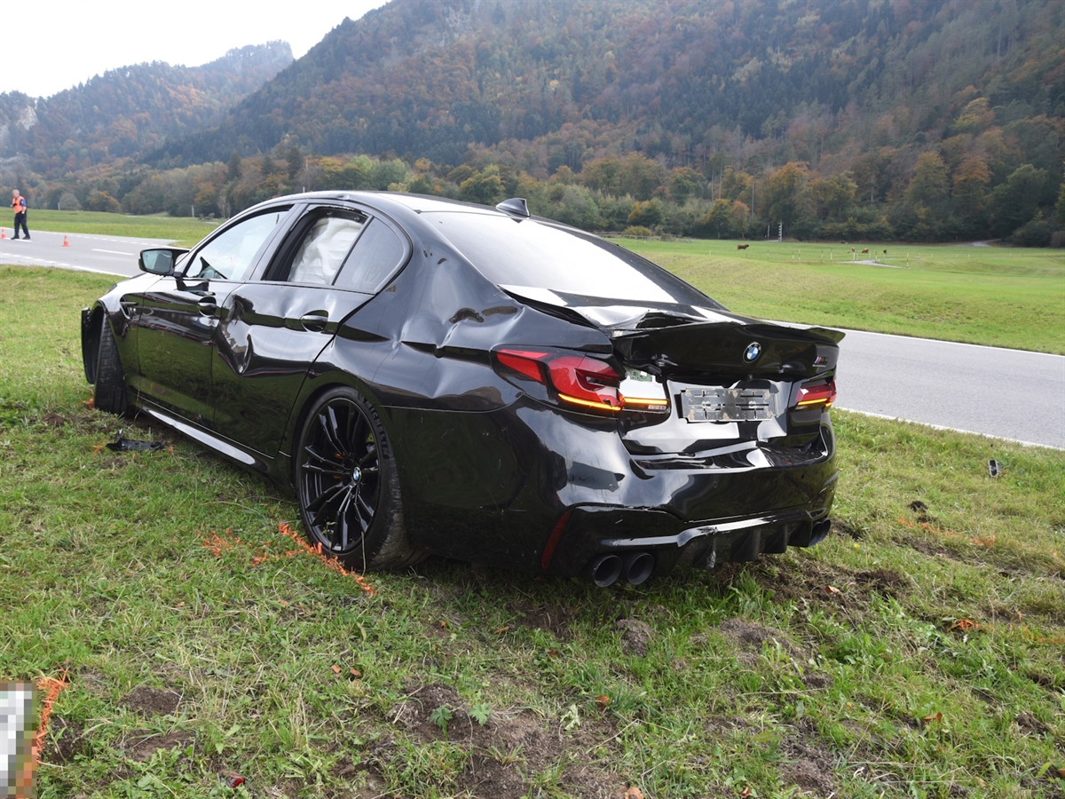 Das Unfallauto, ein schwarzer BMW M5, steht neben der Strasse auf der Weide.