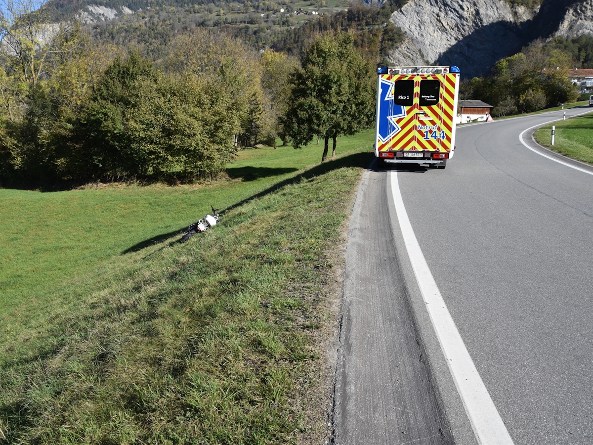 In der abfallenden Wiesenböschung das am Boden liegende Motorrad. Rechts davon auf der Strasse ein Rettungswagen.