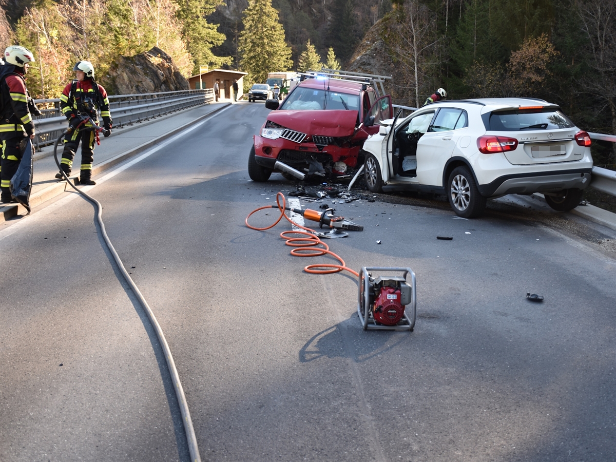 Rechts die beiden kollidierten Fahrzeuge. Beide im Frontbereich total beschädigt. Links davon Einsatzkräfte der Feuerwehr.