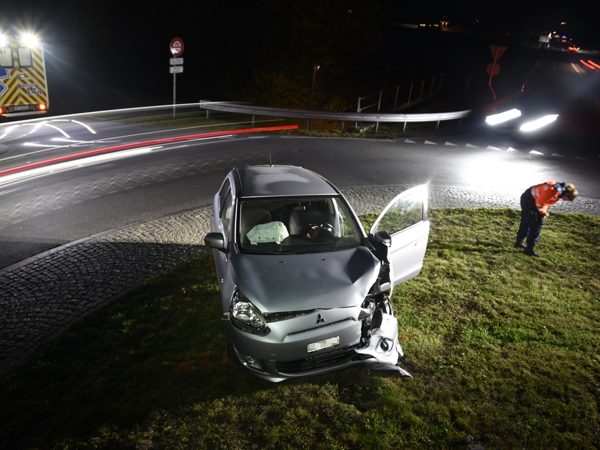 Das frontal beschädigte Auto auf einem Grünstreifen im Kreisel. Links davon ein Rettungswagen, rechts davon eine Polizistin.