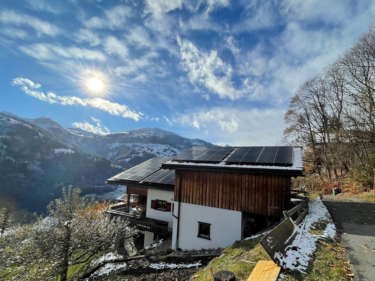 Das Haus mit Solarpanels auf dem Dach. Im Hintergrund Berge und heiterer Himmel.