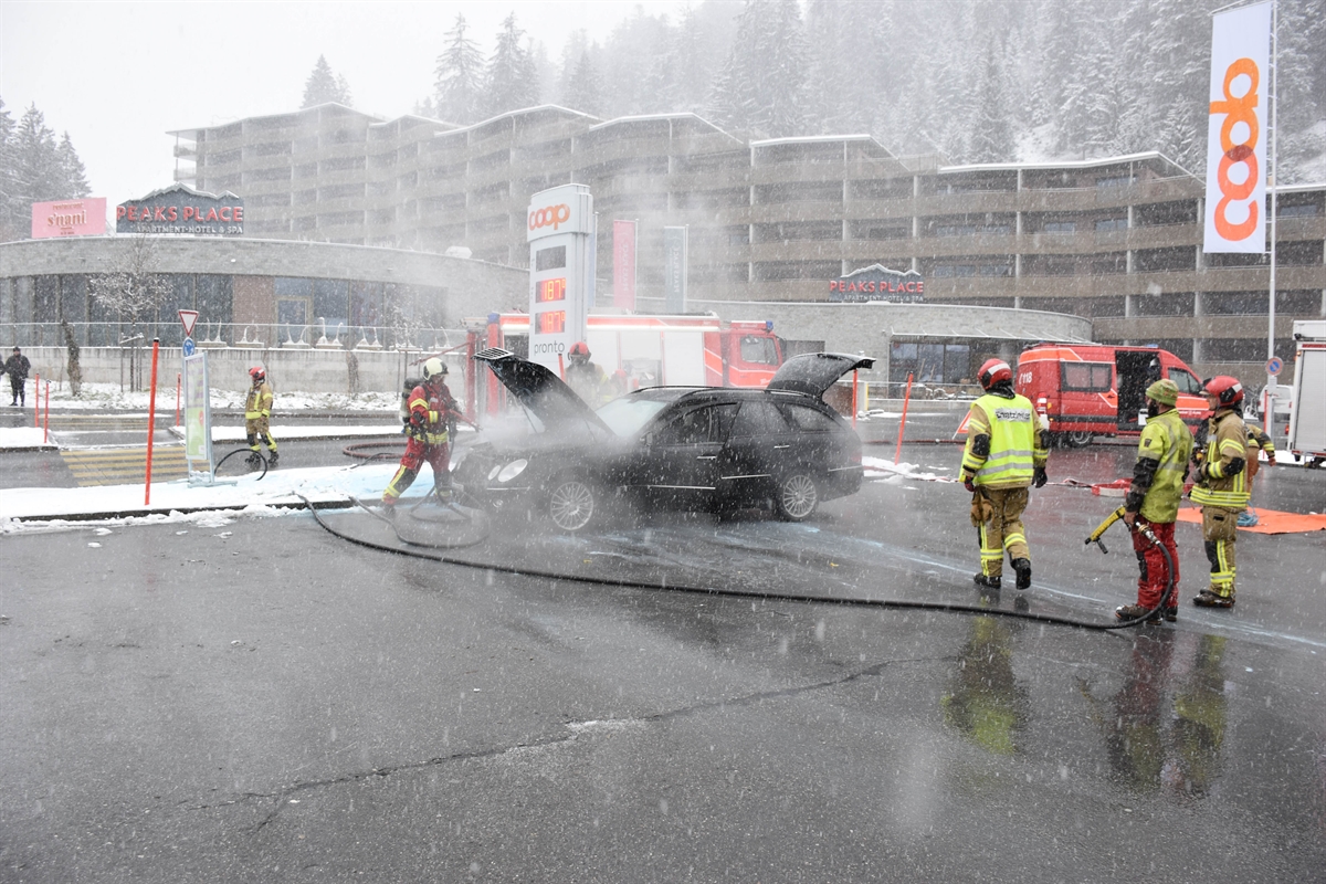 Abgebranntes Auto auf dem Parkplatz vor der Tankstelle mit Feuerwehrleuten und -fahrzeugen