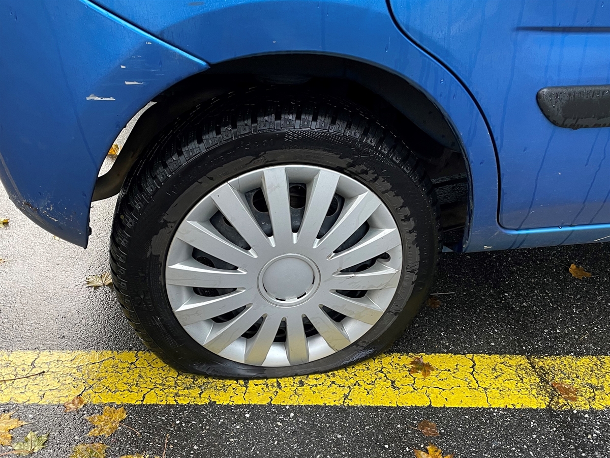 Ein aufgestochener Pneu an einem Auto auf einem Parkplatz.